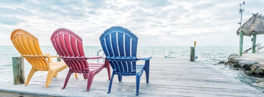 Yellow, Red, and Blue beach chairs on a dock overlooking the ocean